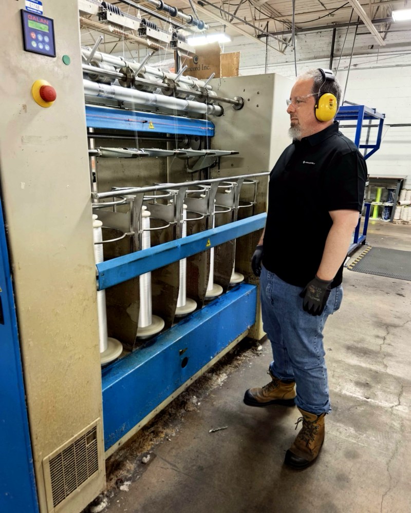 ARMBURY braider room — operator in profile with hearing protection alongside Herzog braiding machines